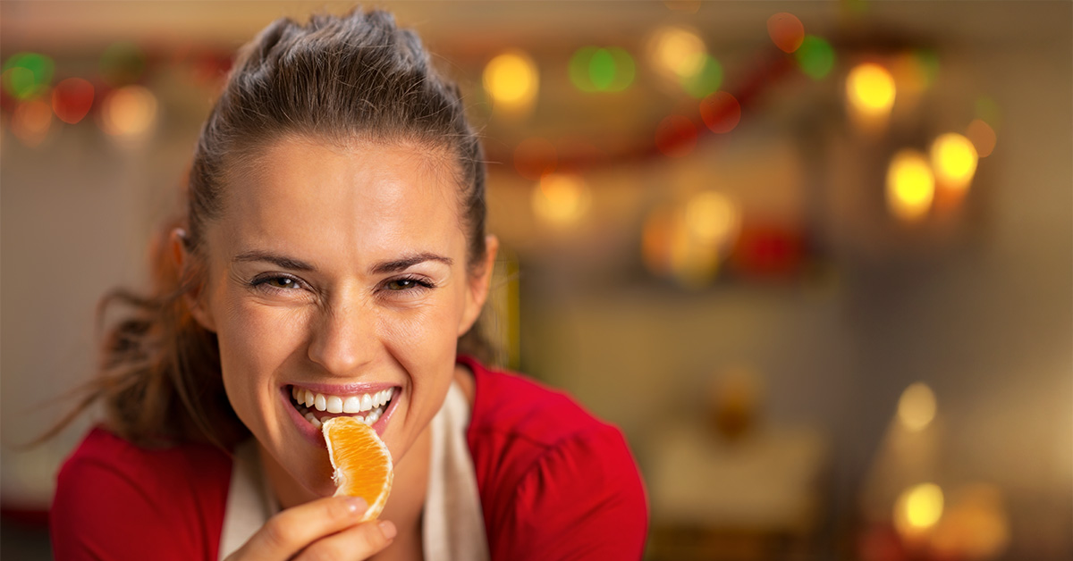 imagem mulher a saborear uma peça de fruta, em ambiente de natal